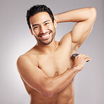 Handsome young mixed race man shirtless in studio isolated against a grey background. Hispanic male using an electric razor to shave his underarms. Healthy and fresh, shaving is part of his grooming