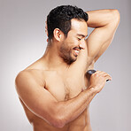 Handsome young mixed race man shirtless in studio isolated against a grey background. Hispanic male using an electric razor to shave his underarms. Healthy and fresh, shaving is part of his grooming