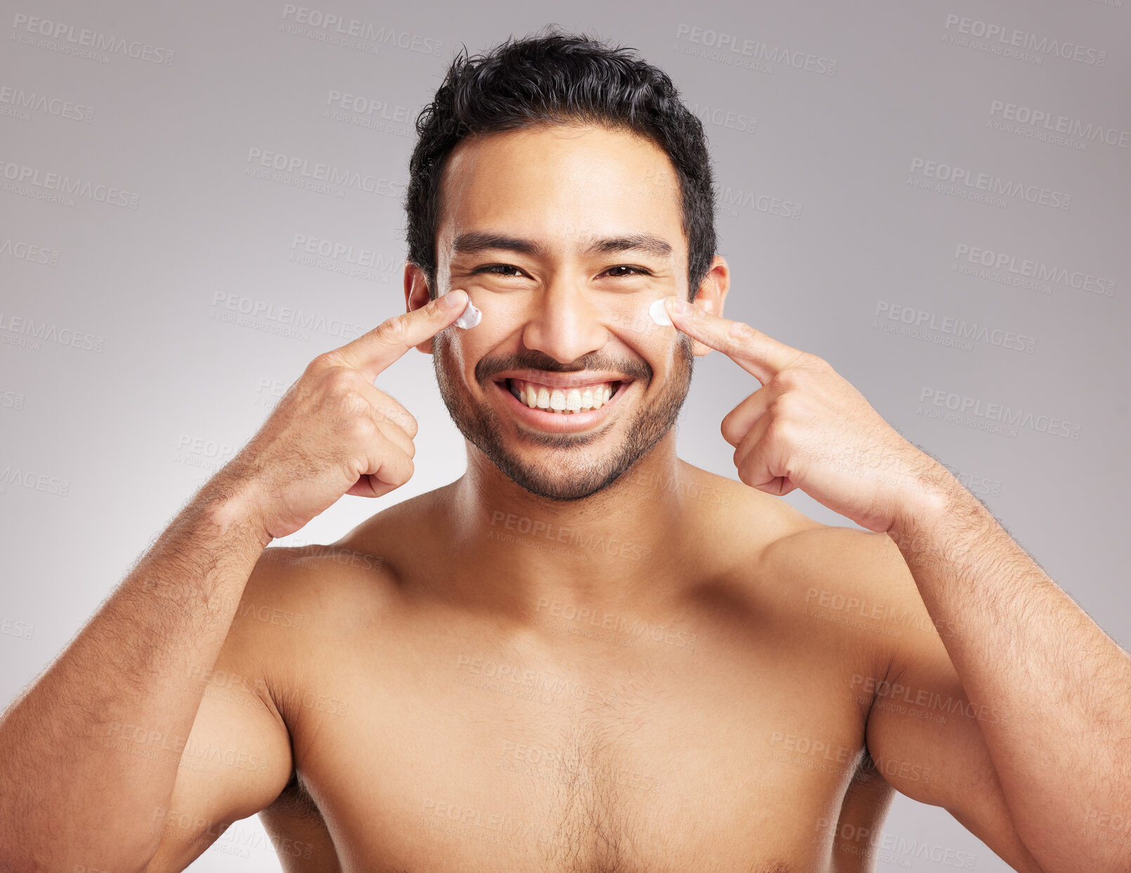 Buy stock photo Handsome young mixed race man shirtless in studio isolated against a grey background. Hispanic male applying moisturizer lotion to his face. Looking confident and happy with his daily skincare regime