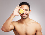 Handsome young mixed race man posing with an orange  slice isolated in studio against a grey background. His skincare regime keeps him fresh. Eating healthy vitamins and nutrients for firm skin