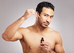 Handsome young mixed race man posing shirtless in studio isolated against a grey background. Hispanic male applying antiaging serum to his face using a dropper. All part of his skincare regime