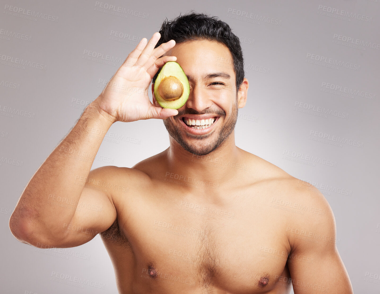 Buy stock photo Handsome young mixed race man posing with an avocado isolated in studio against a grey background. His skincare regime keeps him fresh. For firm skin, eat healthy. Packed with vitamins and nutrients