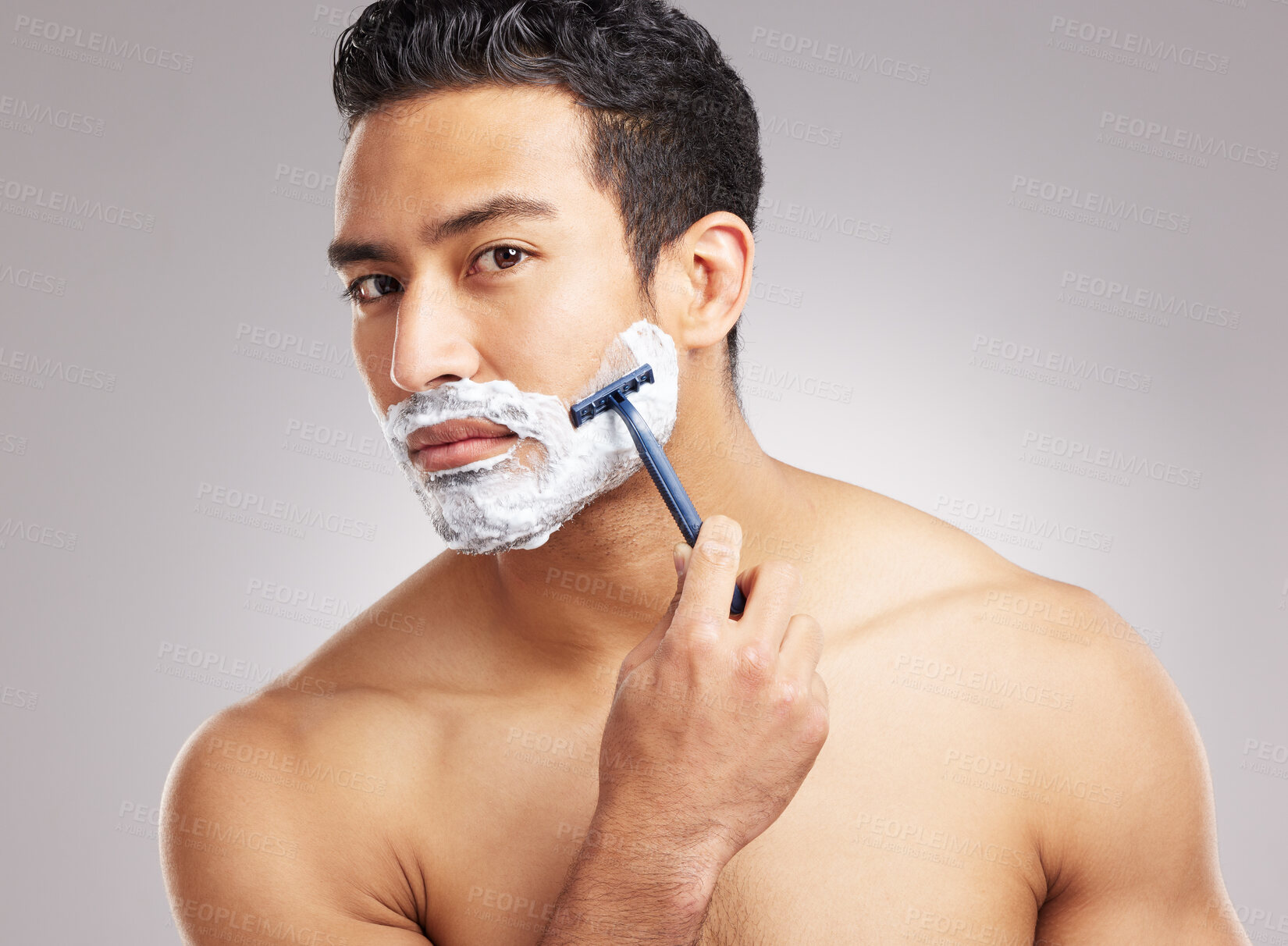 Buy stock photo Handsome young mixed race man shirtless in studio isolated against a grey background. Hispanic male using a razor while shaving. Take care of your skin when you groom or shave your beard and face