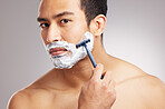 Handsome young mixed race man shirtless in studio isolated against a grey background. Hispanic male using a razor while shaving. Take care of your skin when you groom or shave your beard and face