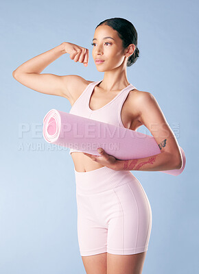 Mixed race fitness woman standing with her yoga mat and flexing her bicep in studio against a blue background. Beautiful young hispanic female athlete exercising or working out. Health and fitness