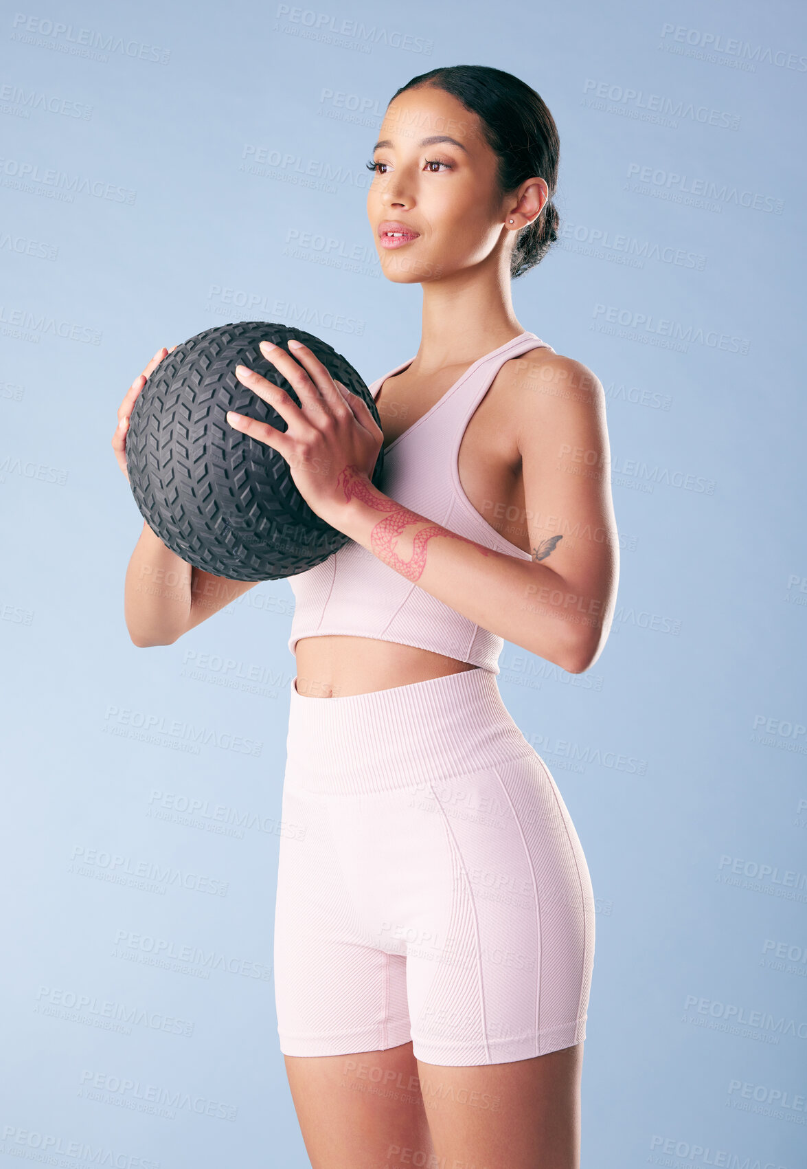 Buy stock photo Mixed race fitness woman standing with a medicine ball or slam ball in studio against a blue background. Beautiful young hispanic female athlete exercising or working out. Health and fitness