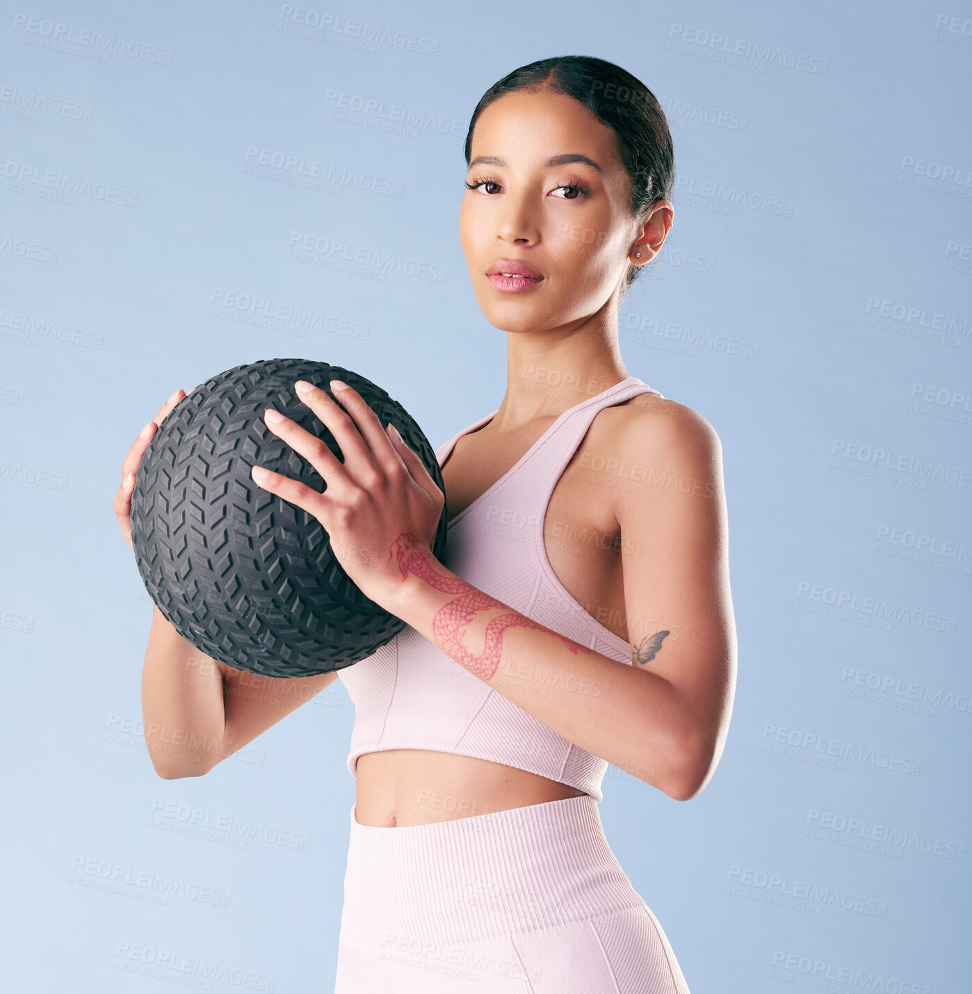 Buy stock photo Mixed race fitness woman standing with a medicine ball or slam ball in studio against a blue background. Beautiful young hispanic female athlete exercising or working out. Health and fitness