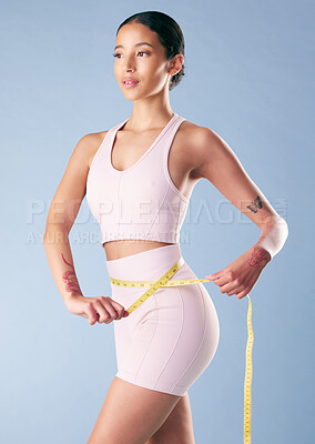 Buy stock photo Mixed race fitness woman posing with a measuring tape around her waist in studio against a blue background. Young hispanic female athlete promoting exercise and a good diet to lose weight and get fit