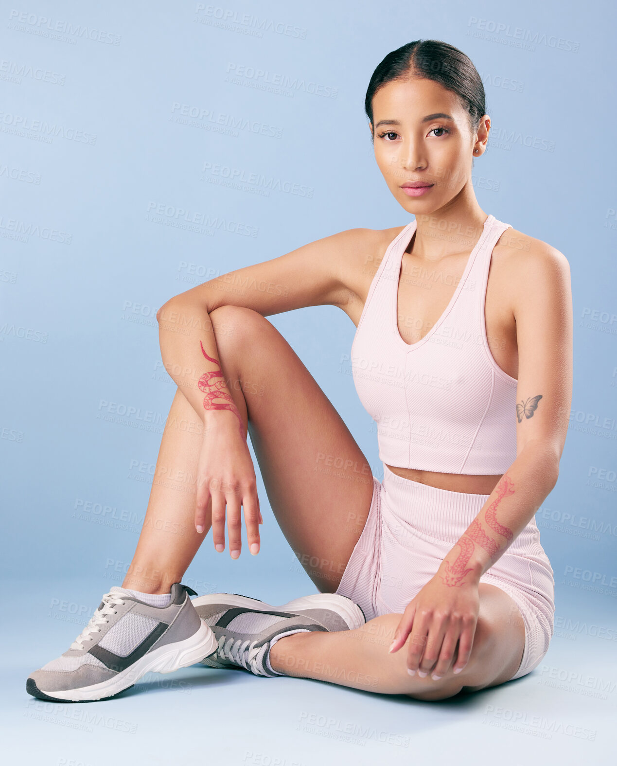 Buy stock photo Mixed race fitness woman sitting during a break from her workout in studio against a blue background. Young hispanic female athlete resting between sets of her exercise routine. Health and fitness