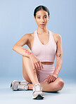 Mixed race fitness woman sitting during a break from her workout in studio against a blue background. Young hispanic female athlete resting between sets of her exercise routine. Health and fitness