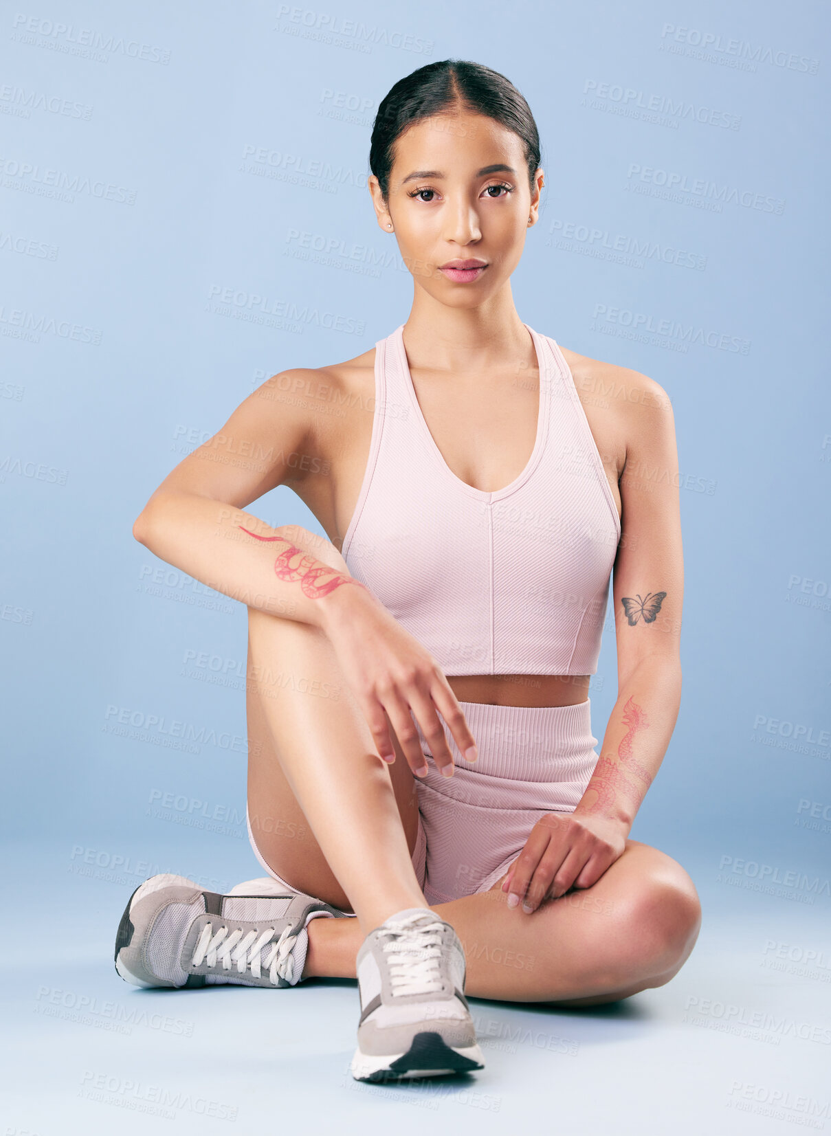 Buy stock photo Mixed race fitness woman sitting during a break from her workout in studio against a blue background. Young hispanic female athlete resting between sets of her exercise routine. Health and fitness