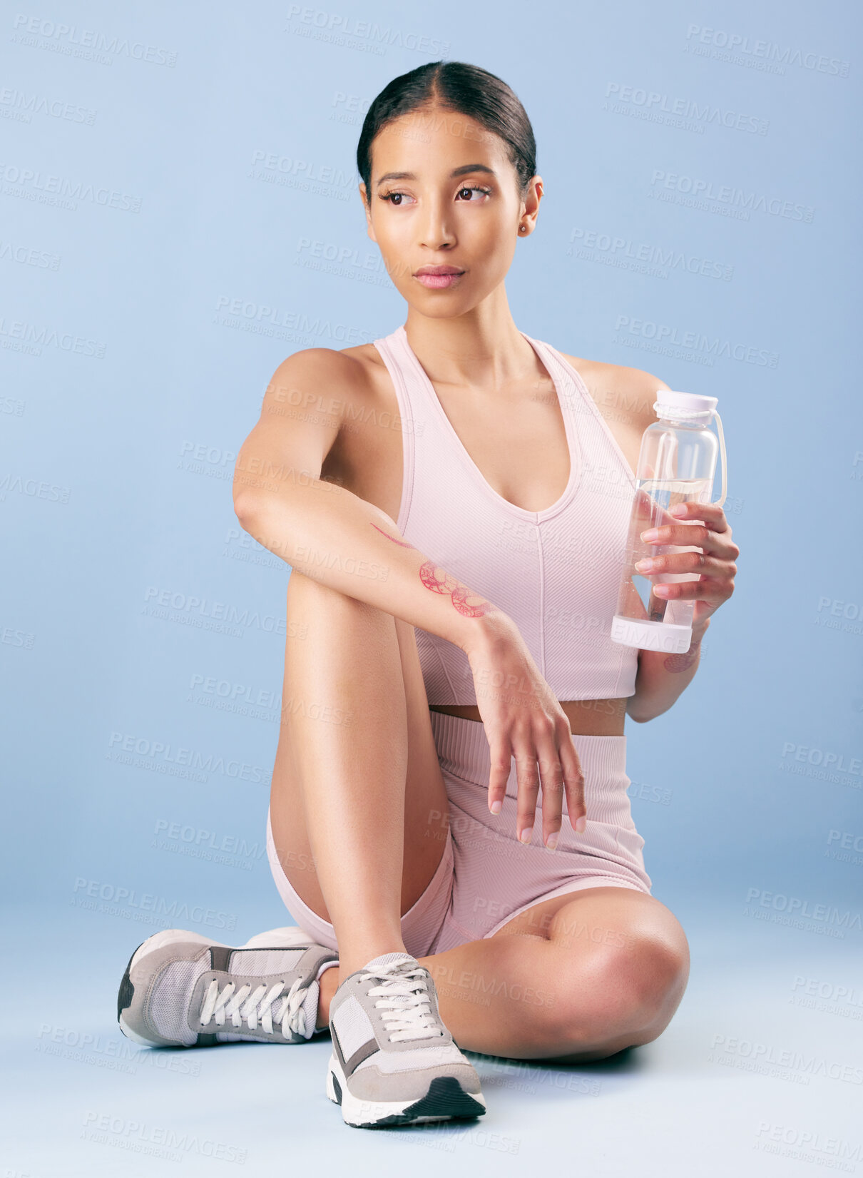 Buy stock photo Mixed race fitness woman sitting during a break from her workout in studio against a blue background. Young hispanic female athlete resting between sets of her exercise routine. Health and fitness