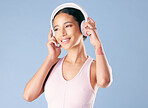 Mixed race fitness woman listening to music on wireless headphones in studio against a blue background. Young hispanic female exercising and working out with her favourite track. Health and fitness