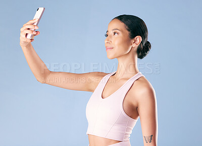 Mixed race fitness woman posing with her phone in studio against a blue background. Young hispanic female athlete taking selfie pictures with her smartphone to track her personal fitness growth