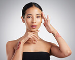 Portrait of a beautiful mixed race woman touching smooth soft skin in a studio. Hispanic model with healthy natural glowing skin looking confident against grey copyspace while doing routine skincare