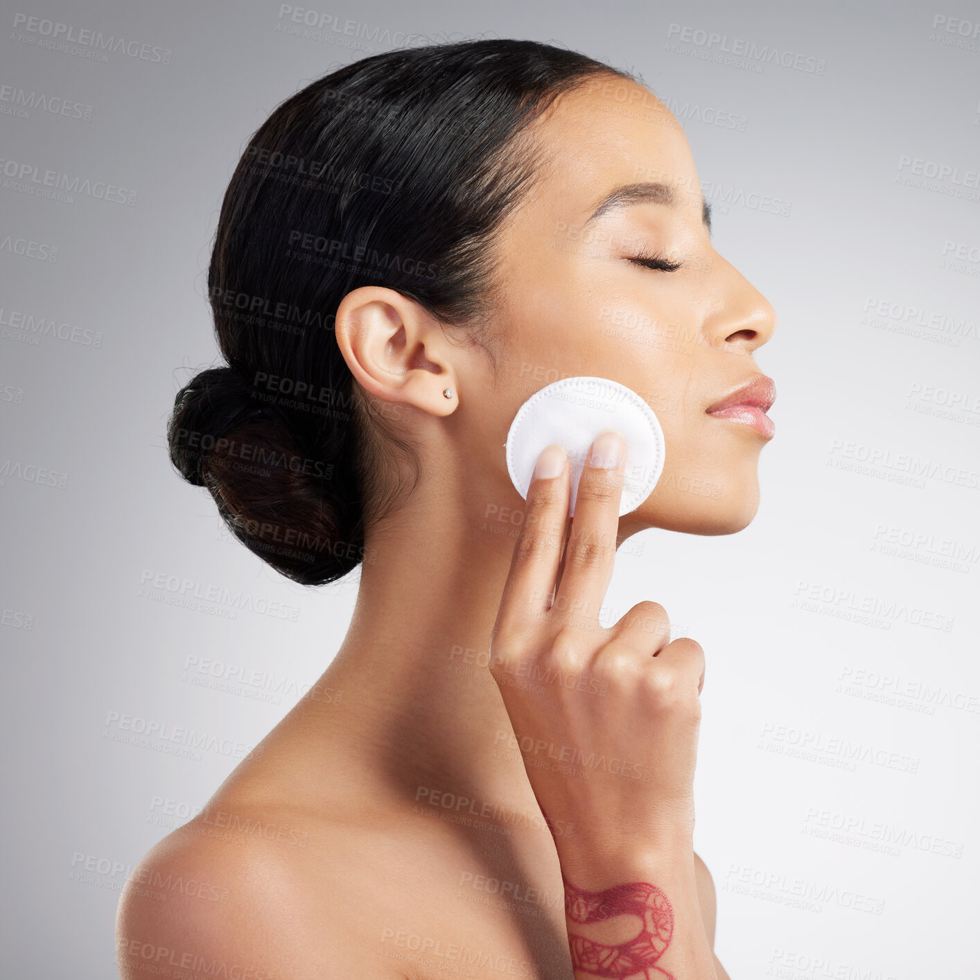 Buy stock photo A beautiful mixed race woman using a cotton pad to remove makeup during a selfcare grooming routine. Hispanic woman applying toner to her face against grey copyspace background in a studio