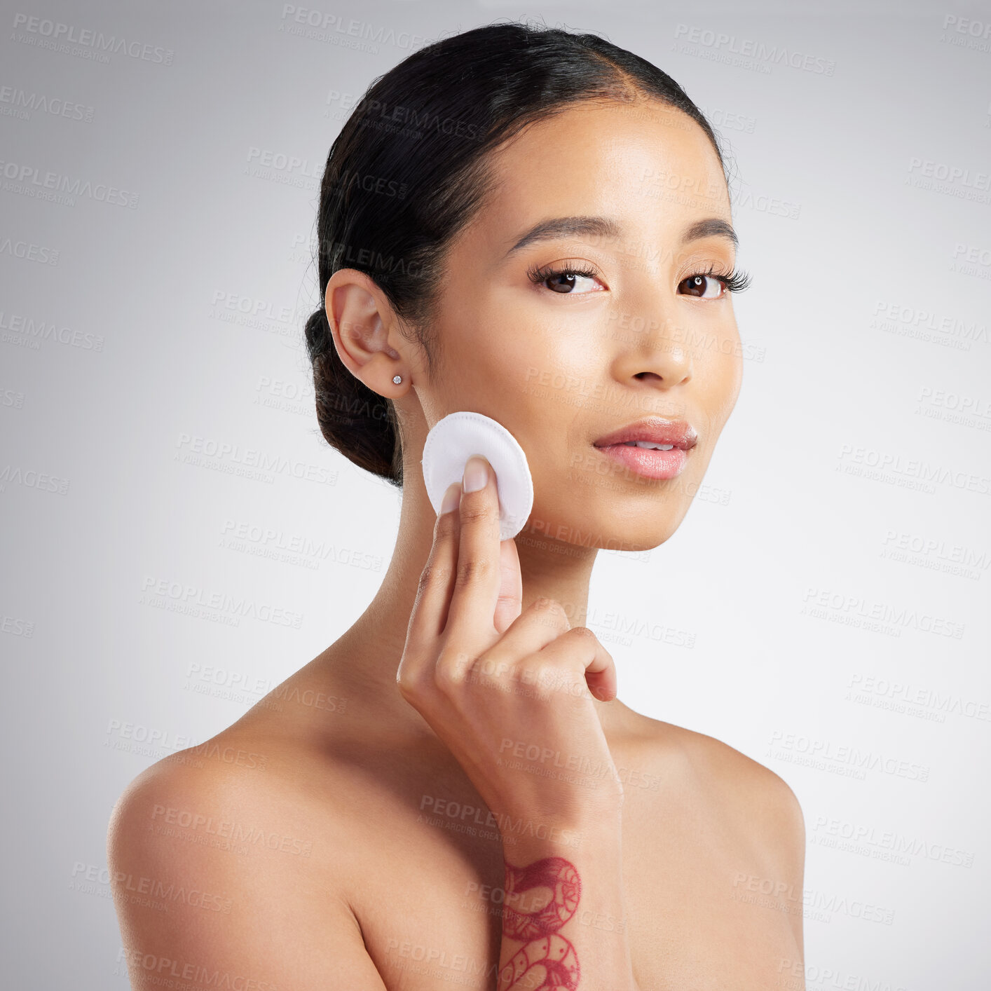 Buy stock photo Studio Portrait of a beautiful mixed race woman using a cotton pad to remove makeup during a selfcare grooming routine. Hispanic woman applying cleanser to her face against grey copyspace background