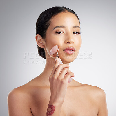 Studio Portrait of a beautiful mixed race woman using a rose quartz derma roller during a selfcare grooming routine. Young hispanic woman using anti ageing tool against grey copyspace background