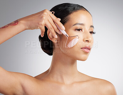 Buy stock photo A beautiful mixed race woman using a rose quartz derma roller during a selfcare grooming routine. Young hispanic woman using anti ageing tool against grey copyspace background