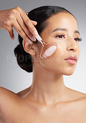 Buy stock photo Studio closeup of a beautiful mixed race woman using a rose quartz derma roller during a selfcare grooming routine. Young hispanic woman using anti ageing tool against grey copyspace background