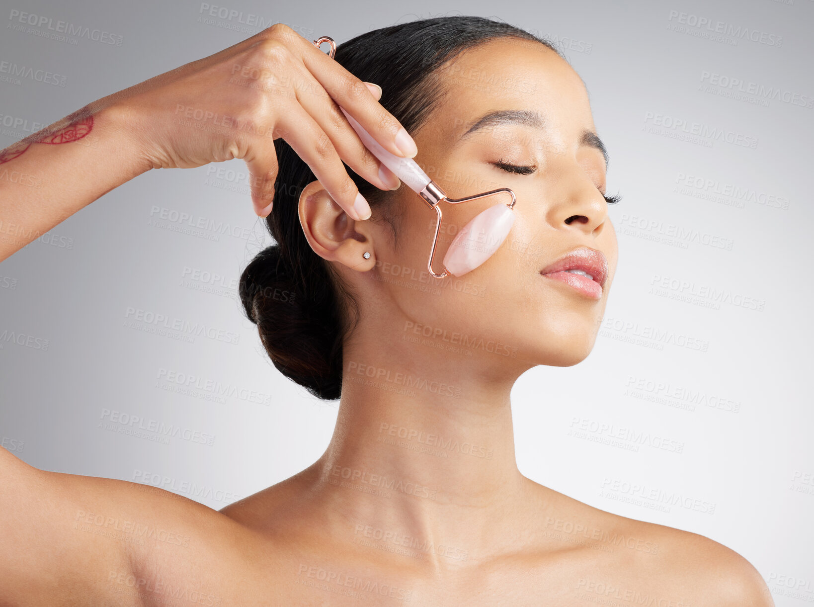 Buy stock photo A beautiful mixed race woman using a rose quartz derma roller during a selfcare grooming routine. Young hispanic woman using anti ageing tool against grey copyspace background