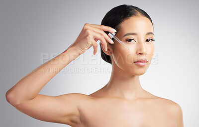 Studio Portrait of a beautiful mixed race woman applying a soothing face serum to her radiant smooth face while posing against a grey background. Hispanic woman with flawless skin using essential oil