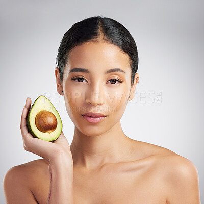 Studio Portrait of a beautiful young mixed race woman holding a sliced avocado. Hispanic model with glowing skin holding a fruit against a grey copyspace background