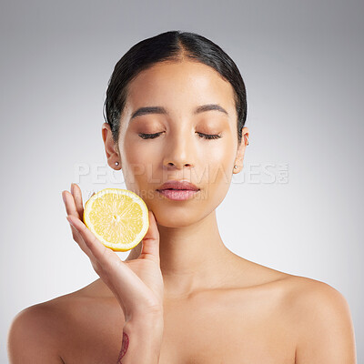 A beautiful young mixed race woman holding a lemon. Hispanic model using a lemon to reduce acne against a grey copyspace background