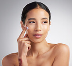 A beautiful smiling mixed race woman applying cream to her cheek. Hispanic model with glowing skin using sunscreen against a grey copyspace background