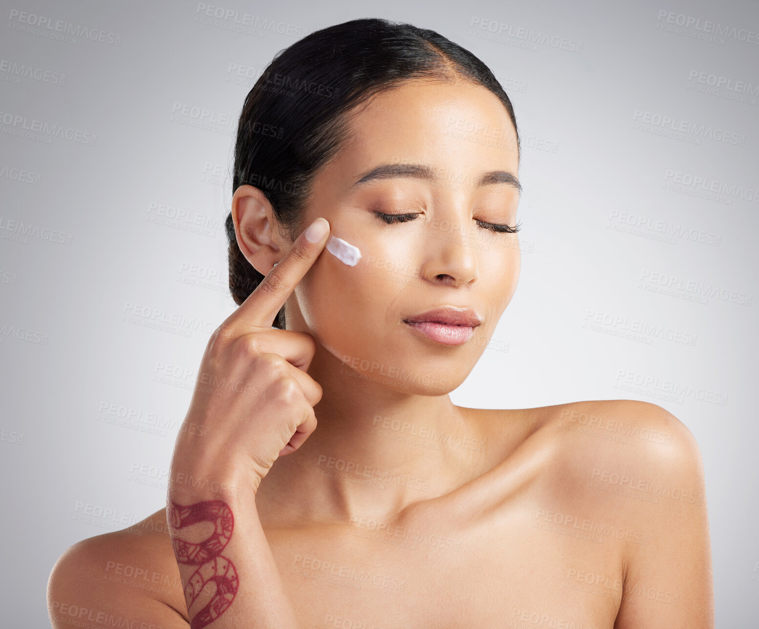 Buy stock photo A beautiful smiling mixed race woman applying cream to her cheek. Hispanic model with glowing skin using sunscreen against a grey copyspace background