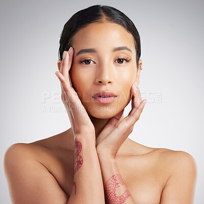 Studio portrait of a beautiful mixed race woman touching smooth soft skin in a studio. Hispanic model with healthy natural glowing skin looking confident against grey copyspace while doing routine skincare