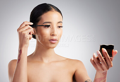 A beautiful young mixed race woman with glowing skin posing against grey copyspace background. Hispanic woman with natural looking eyelash extensions applying mascara in a mirror