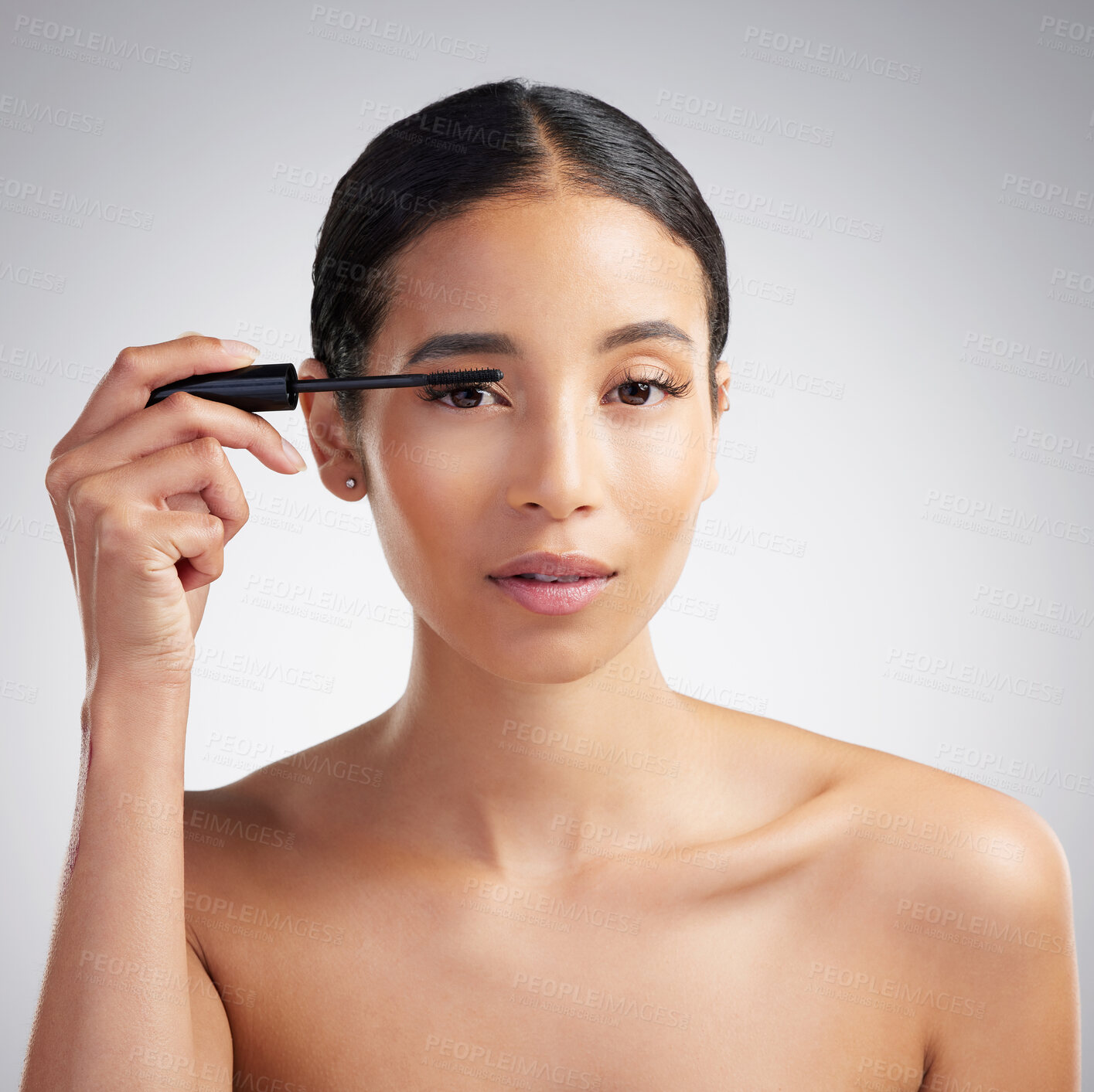 Buy stock photo Studio portrait of a beautiful young mixed race woman with glowing skin posing against grey copyspace background. Hispanic woman with natural looking eyelash extensions applying mascara