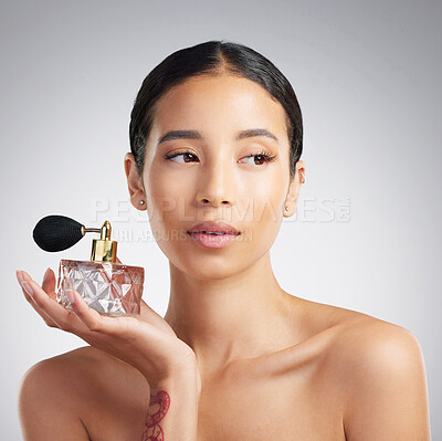 A beautiful young mixed race woman with glowing skin posing against grey copyspace background while holding a bottle of perfume. Hispanic woman applying perfume to her skin
