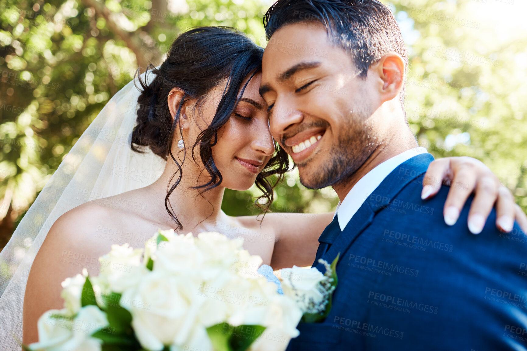 Buy stock photo Loving bride and groom hugging and sharing romantic moment on their wedding day. Happy romantic couple posing together against nature background