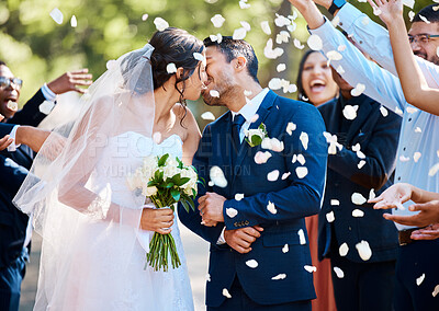 Buy stock photo Newlywed couple bride and groom sharing a kiss while surrounded by friends and family and being showered with confetti rose petals after their wedding ceremony