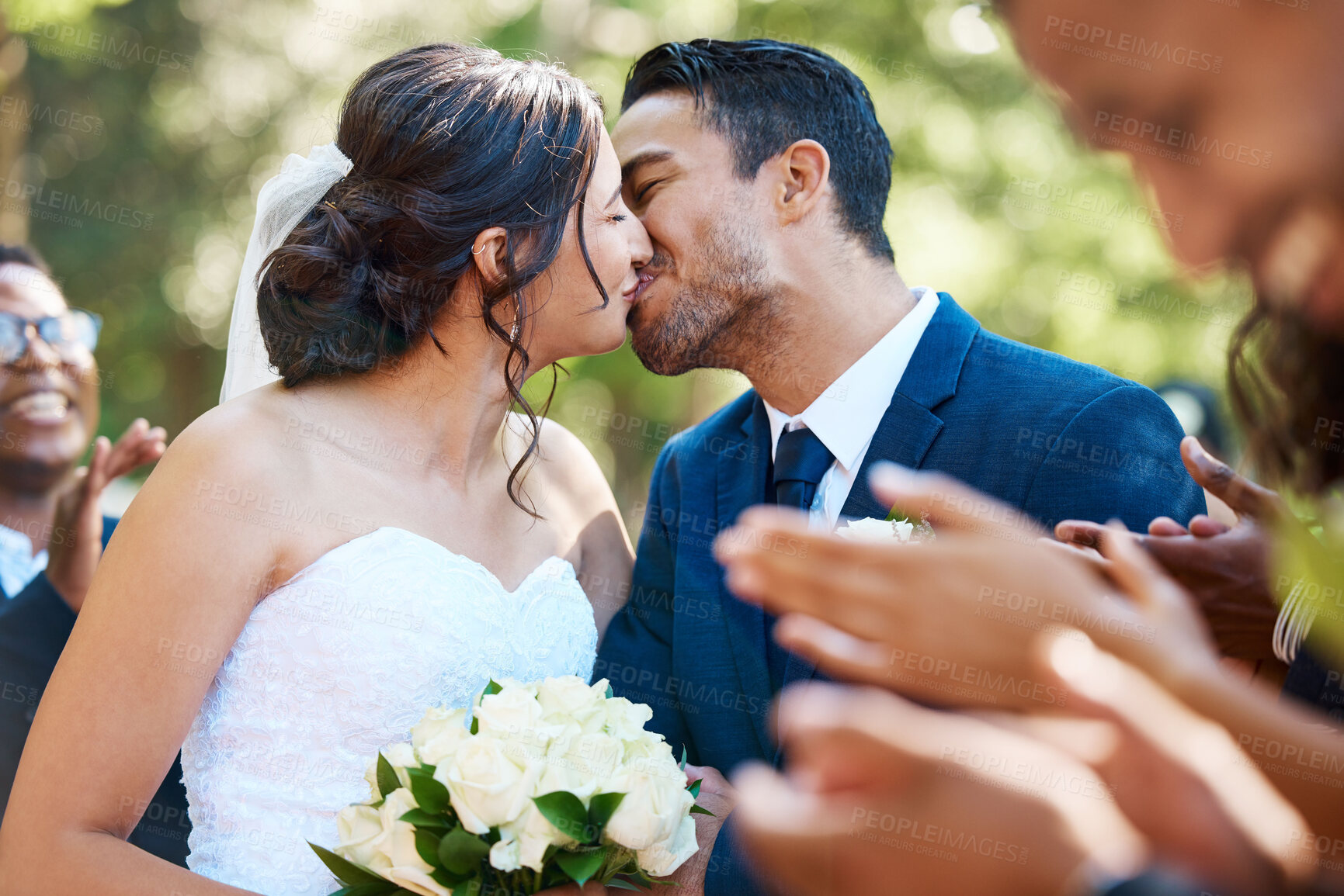 Buy stock photo Happy romantic newlywed couple kissing outside while surrounded by friends and family on their wedding day. Bride and groom deeply in love