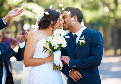 Buy stock photo Happy bride and groom sharing a kiss while surrounded by guests and being showered with confetti rose petals after wedding ceremony
