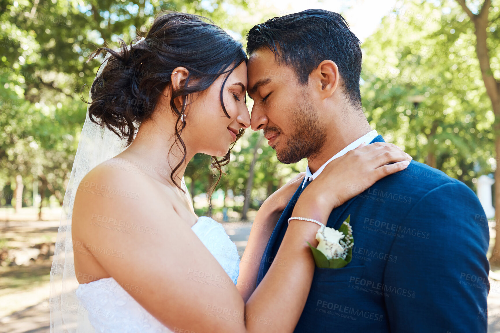 Buy stock photo Bride and groom standing together and touching foreheads while standing together on their wedding day. Newlywed couple sharing romantic moment outdoors