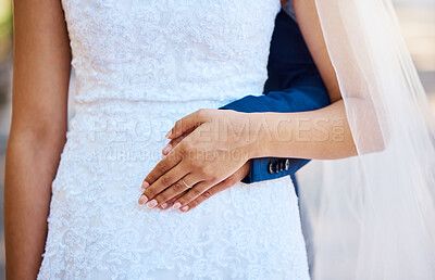 Close up of a bride and groom posing together. Woman placing her hand on her husbands as they stand together. Bride in beautiful white dress