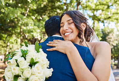 Beautiful joyful bride holding bouquet and embracing her husband. Happy newlywed couple hugging and looking happy on their wedding day against nature background