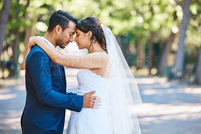 Young bride and groom enjoying romantic moments outside on a beautiful summer day in nature. Newlywed couple touching foreheads while standing close