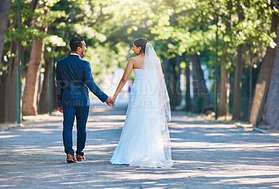 Buy stock photo Rear view shot of newlywed couple holding hands and walking through park. Bride and groom walking away after their wedding reception. Living happily ever after