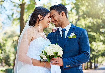 Buy stock photo Happy romantic couple standing together holding a bouquet and touching foreheads while posing together on their wedding day