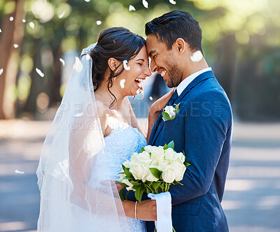 Buy stock photo Happy young couple on their wedding day being showered with confetti. Husband and wife standing face to face and enjoying romantic moments in nature