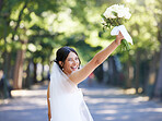 Cheerful bride standing outside and lifting her wedding bouquet. Bride getting ready to throw bouquet celebrating wedding tradition