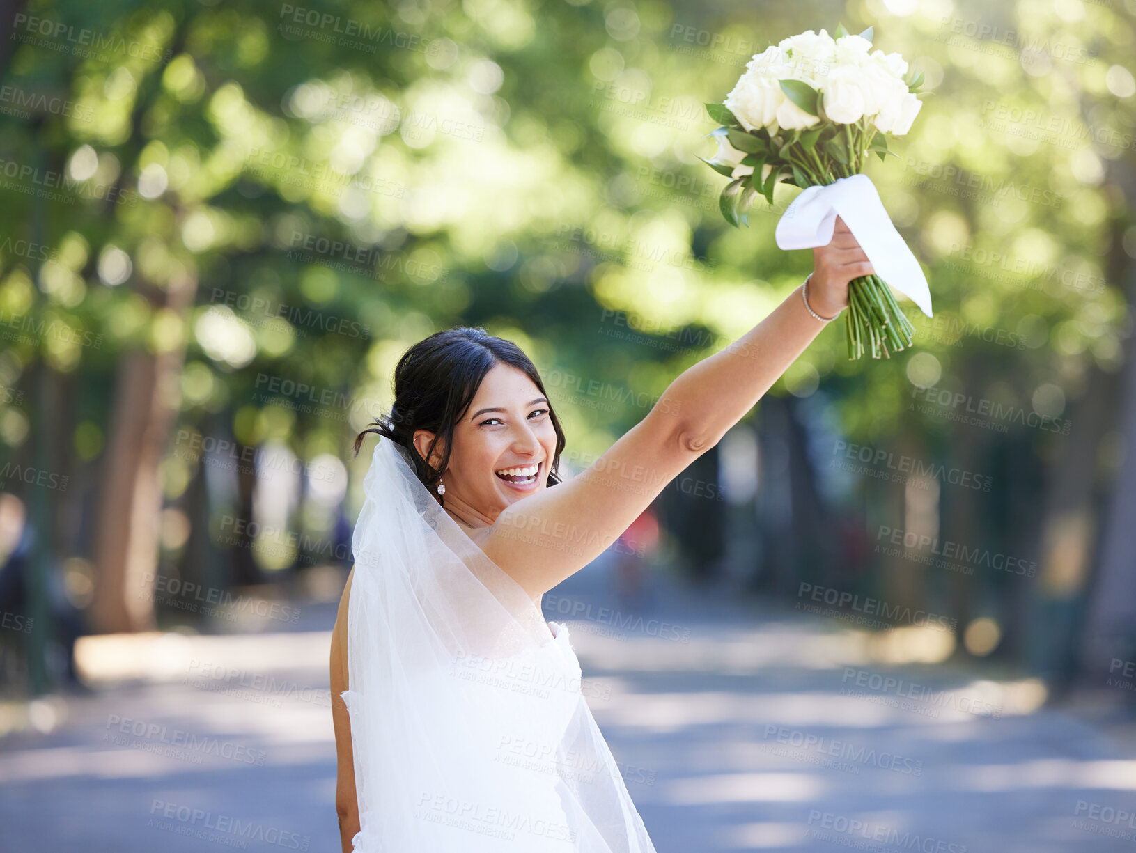 Buy stock photo Cheerful bride standing outside and lifting her wedding bouquet. Bride getting ready to throw bouquet celebrating wedding tradition