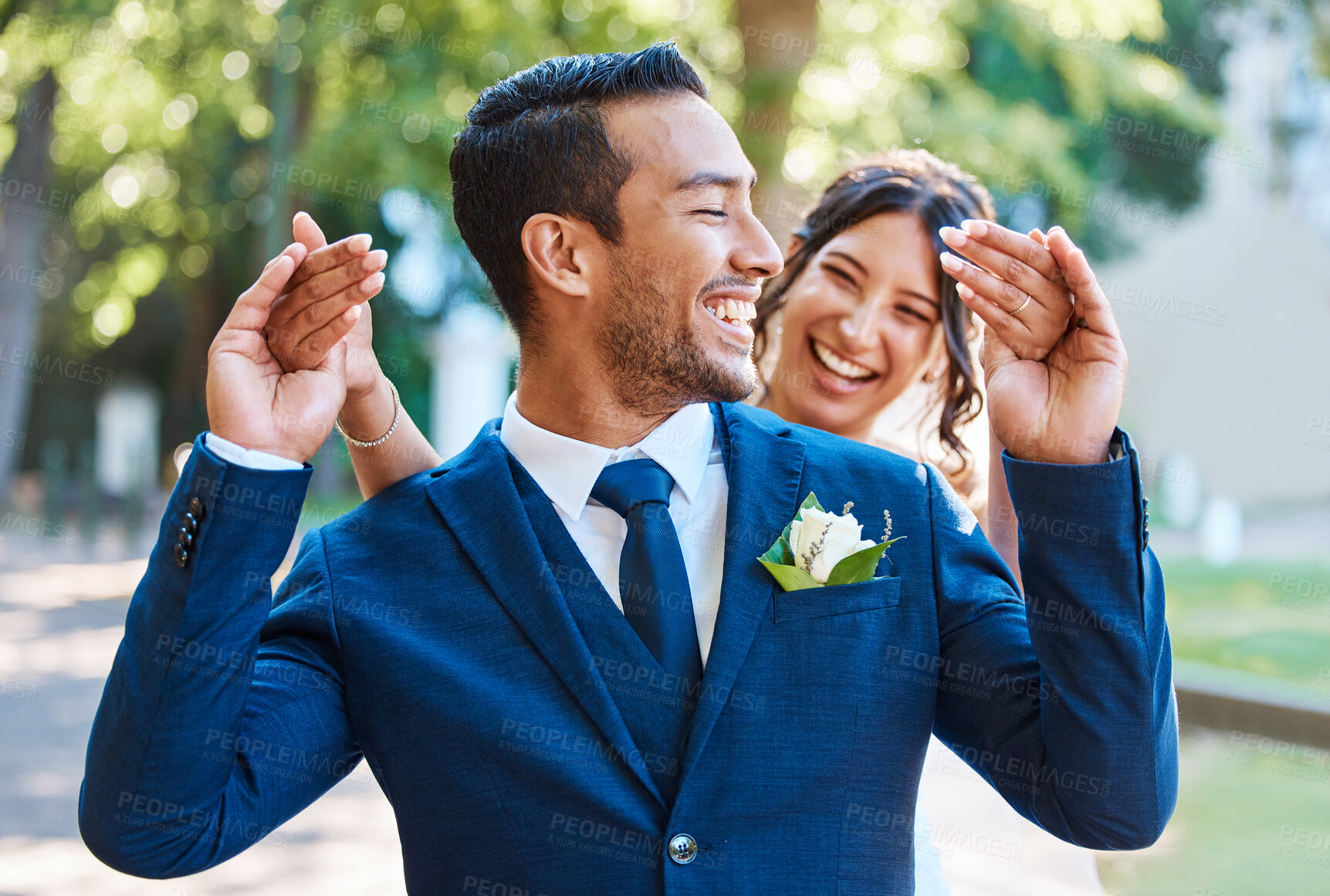 Buy stock photo Playful mixed race newlywed couple standing outside and having fun on their wedding day. Beautiful bride surprising her groom