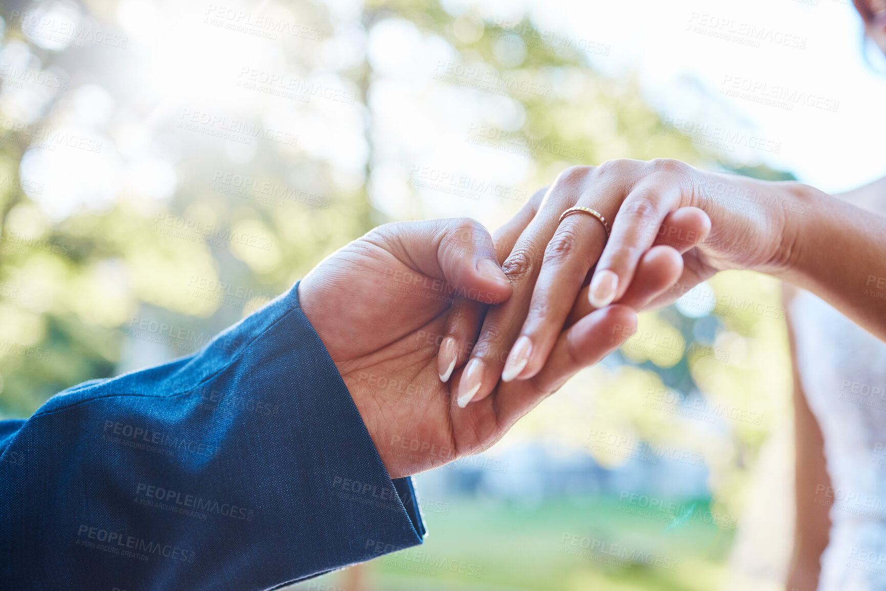 Buy stock photo Close up hands of newlywed couple standing outside on a sunny day. Groom holding his brides hand with wedding band. Groom about to put ring in brides finger