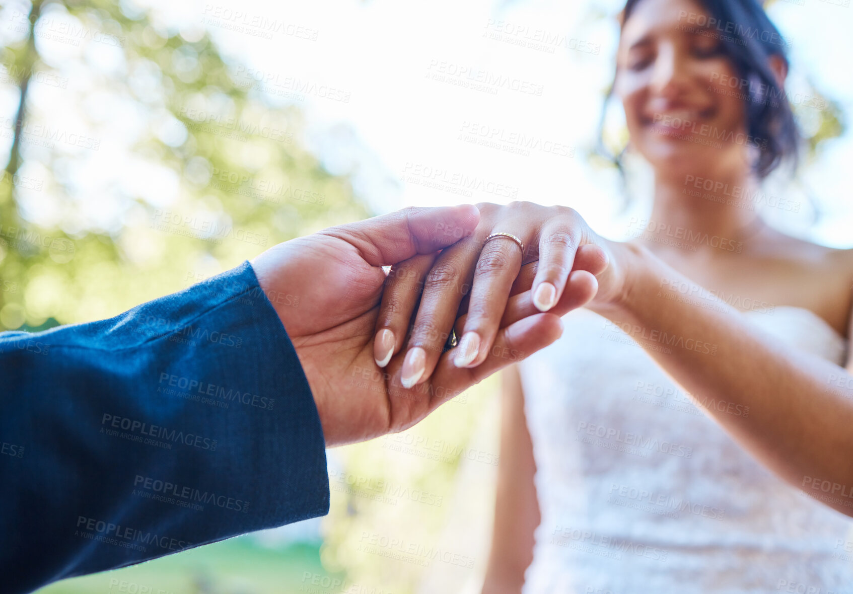 Buy stock photo Close up hands of newlywed couple standing outside on a sunny day. Groom holding his brides hand with wedding band. Groom about to put ring in brides finger